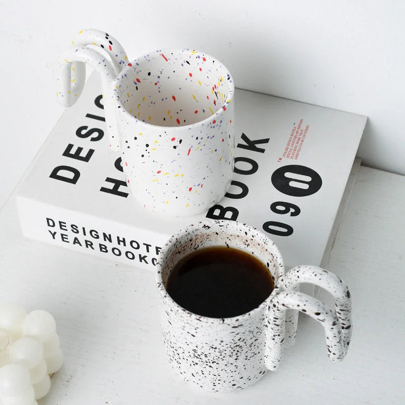 Confetti Splatter and Black Splatter ceramic mugs with loop handles on a design book - RoomDen