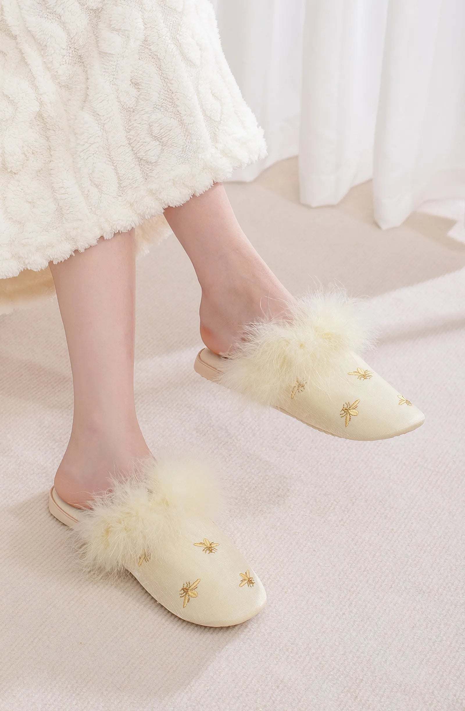 Side view of Beige satin slippers with gold bee detail worn on feet - RoomDen