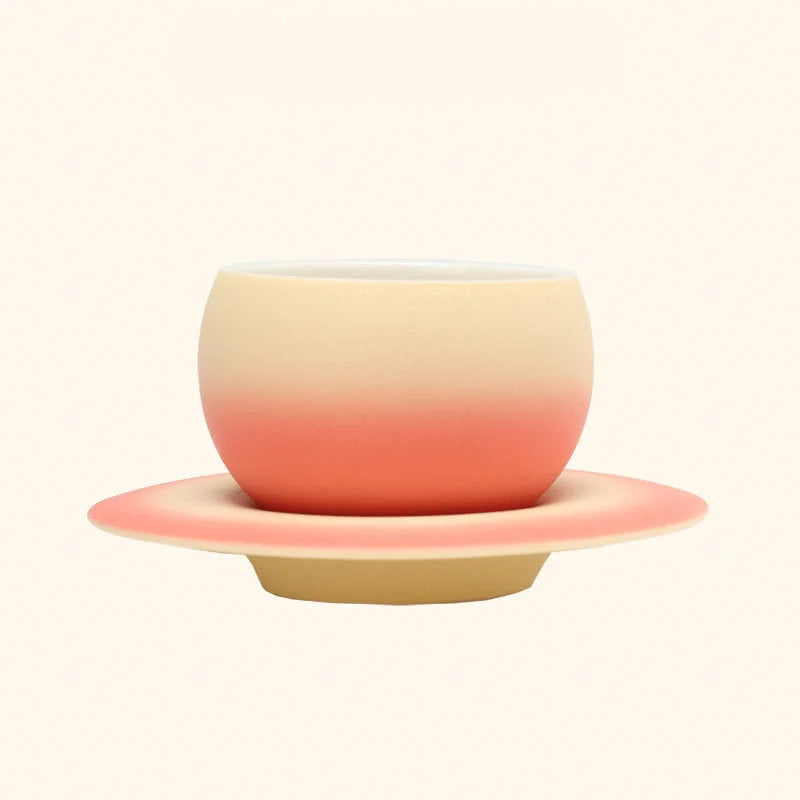 The Peach Sorbet Ombre Ceramic Cup displayed on its matching Saturn-ring saucer. - RoomDen