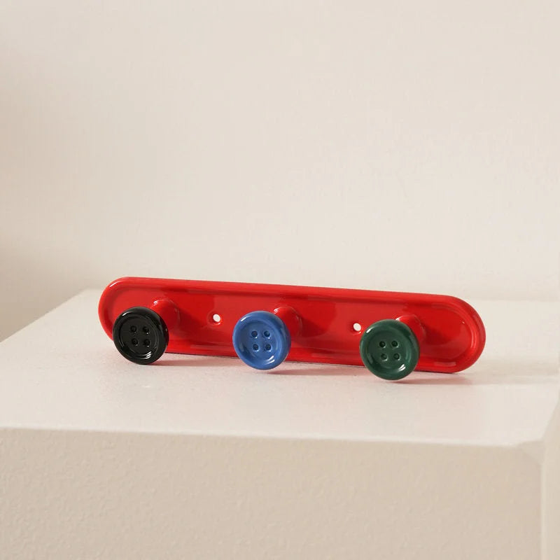 Red 3-hook button ceramic wall rack with colorful buttons on a white surface. - RoomDen