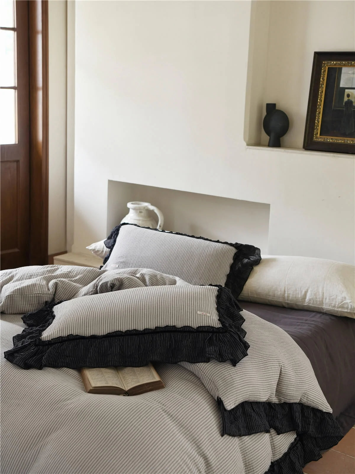 Angled view of the pinstripe pillows with black ruffle detail on a neatly made bed. - RoomDen