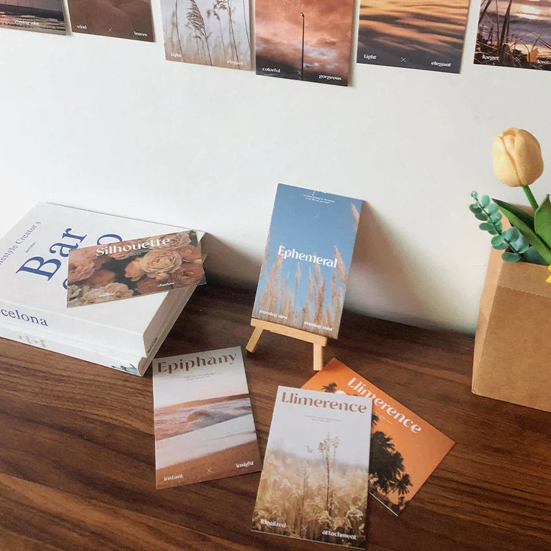 Several cards from the Sunset Hues collage kit displayed on a wooden desk next to a book and a yellow tulip, showing their matte texture - RoomDen.
