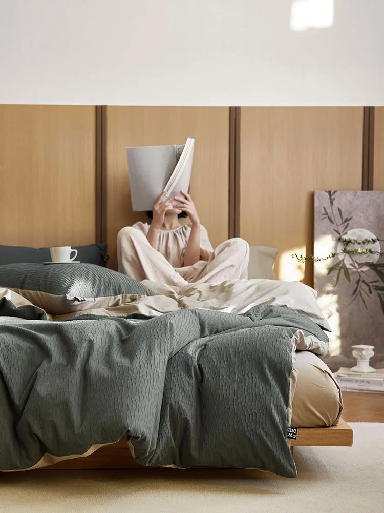 A person sitting in bed reading, covered by the Slate Grey Wavy Textured duvet cover. - RoomDen