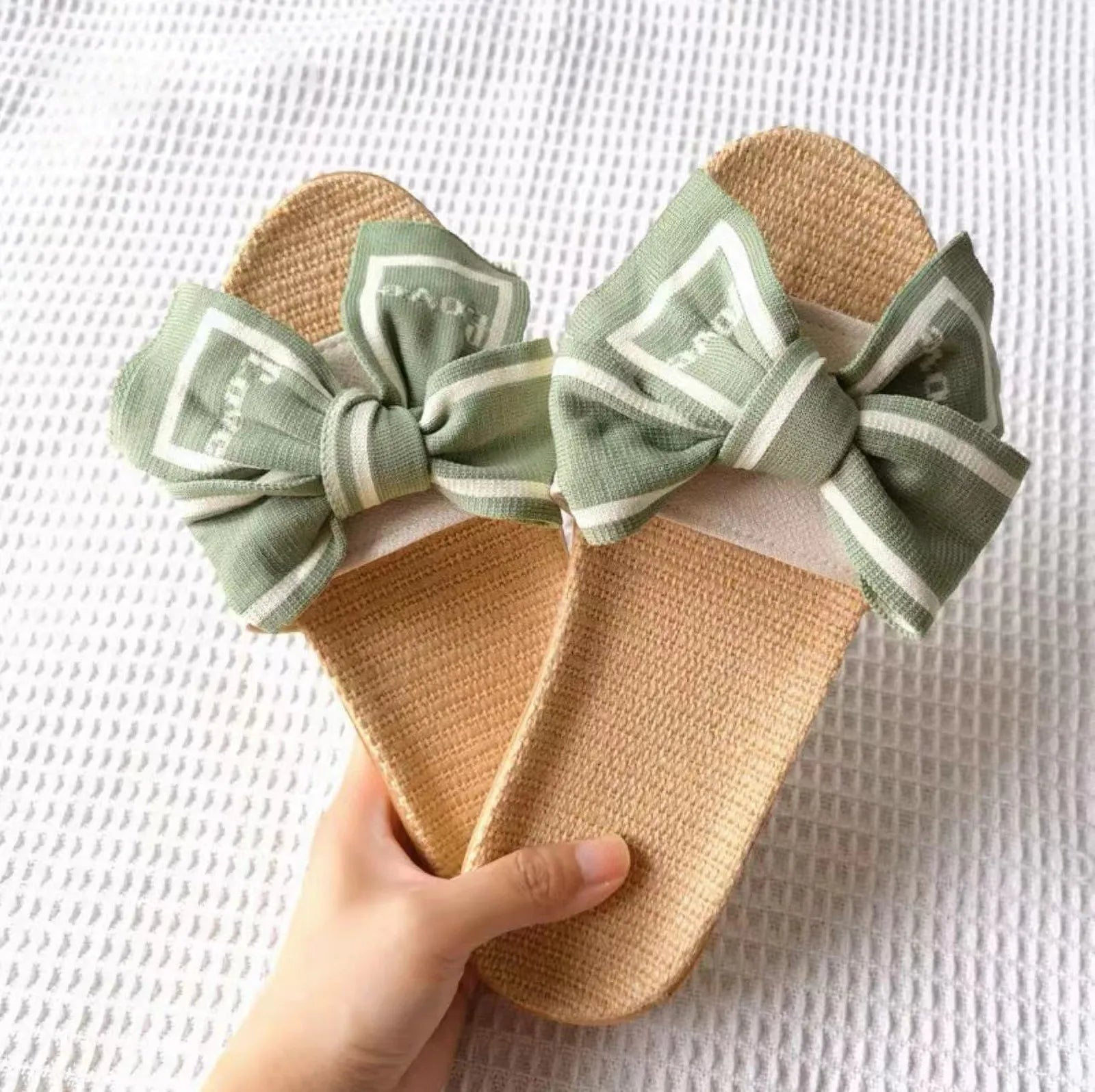 Hand holding pair of Sage Green "Love" Bow Linen House Slippers - RoomDen