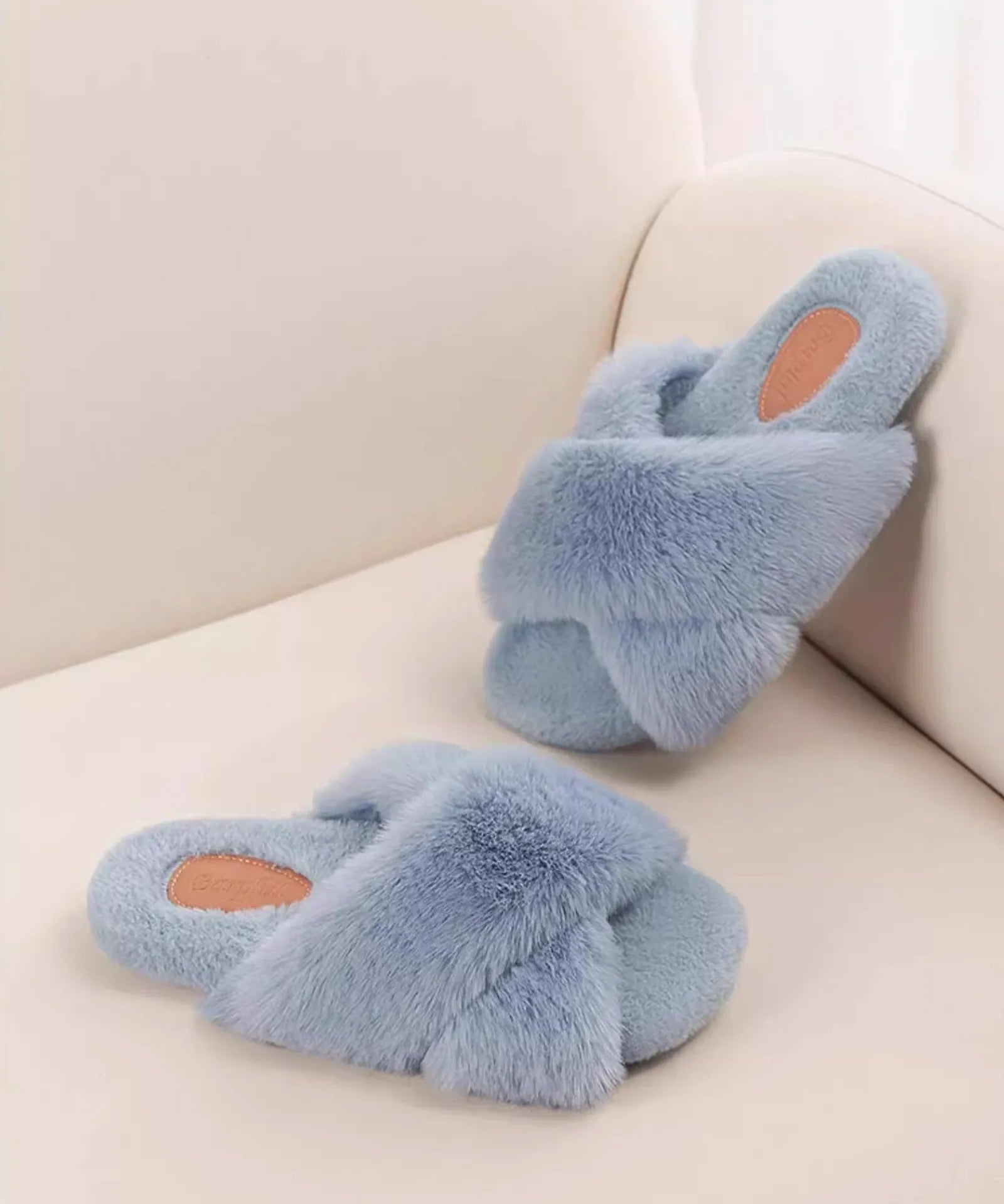 Blue fluffy house slippers resting on a cream sofa - RoomDen