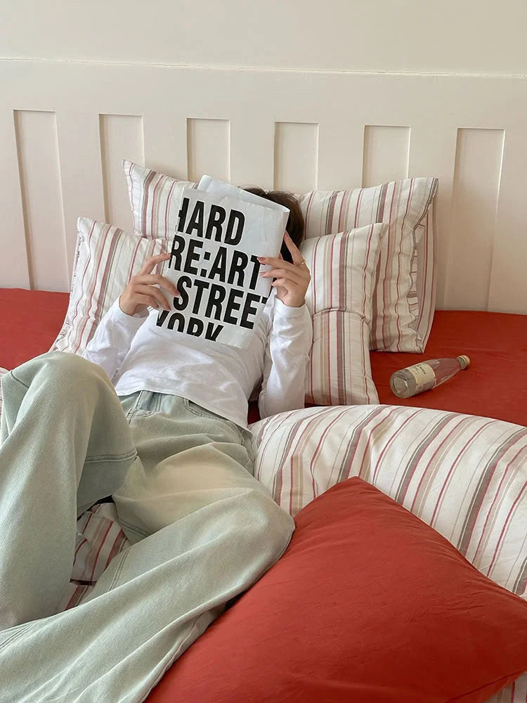 A person relaxing in bed with the Red Striped Washed Cotton Bedding Set. - RoomDen