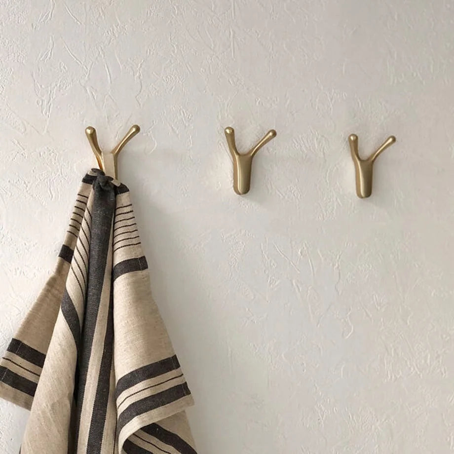 Front view of three gold branch-shaped decorative hooks, one holding a beige and black striped towel - RoomDen