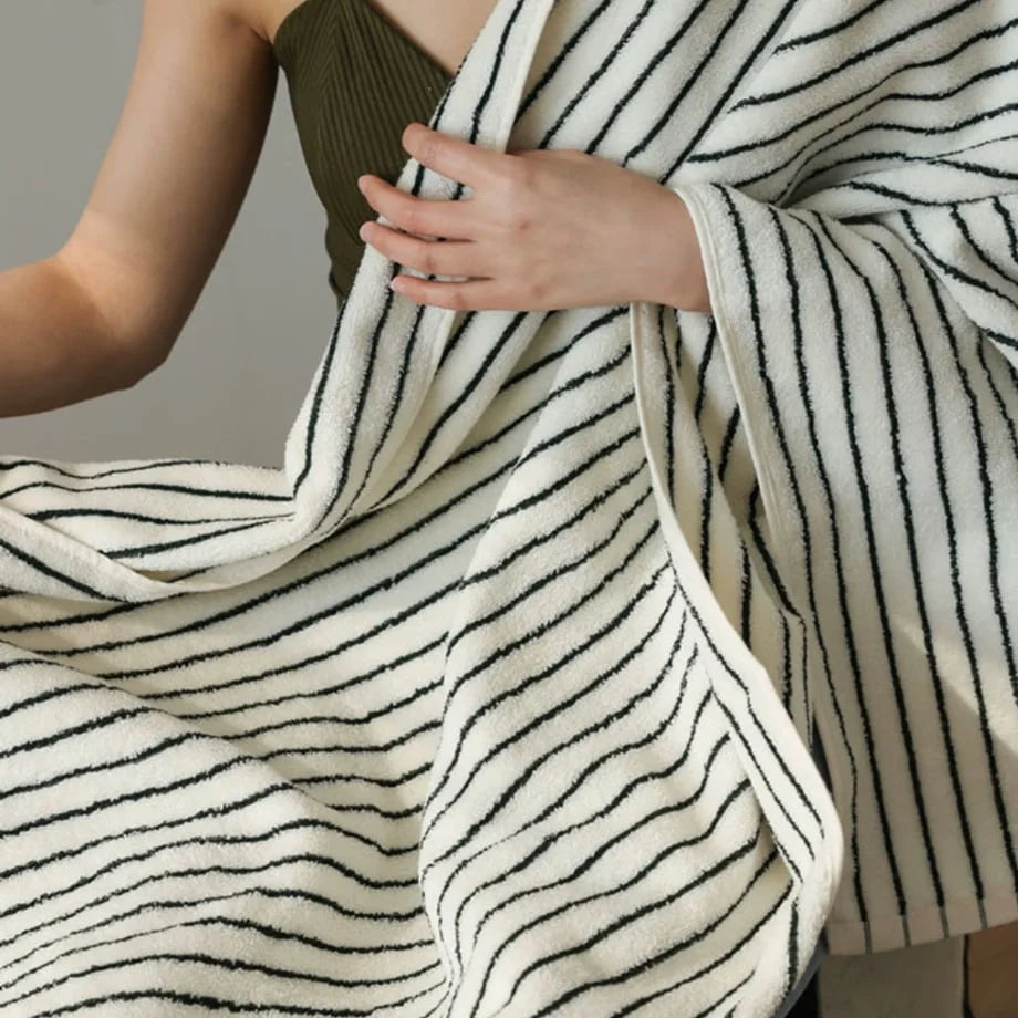 Close-up of a woman wrapping herself in a soft, textured striped cotton bath towel.