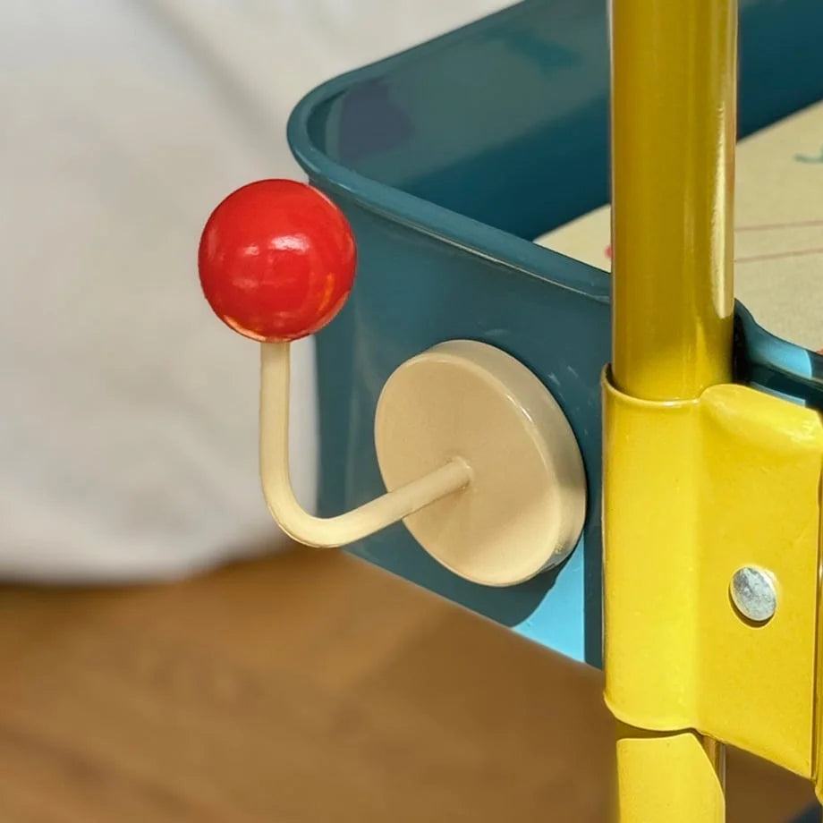 The Red & Beige Metal Hook shown on the side of a teal cart tier near a sunlit wall - RoomDen.