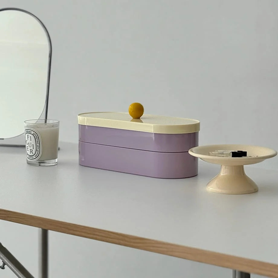 Smooth Colorblock ABS Makeup Organizer in lavender and cream, shown on a white vanity next to a candle and mirror - RoomDen.