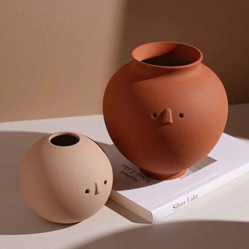 A close-up of the Pot and Ball Frosted Minimalist Face Vases styled on a white book. - RoomDen