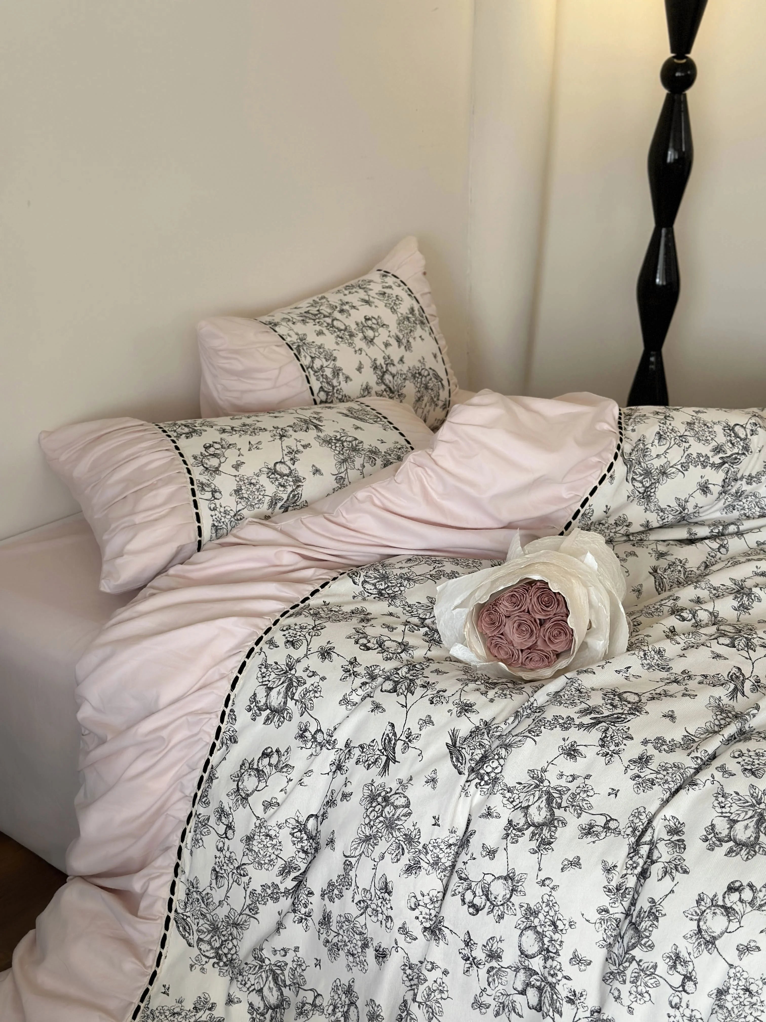 The Ruffled Botanical Toile Bedding Set shown in the Pink Toile color variant with a bouquet of pink roses. - RoomDen