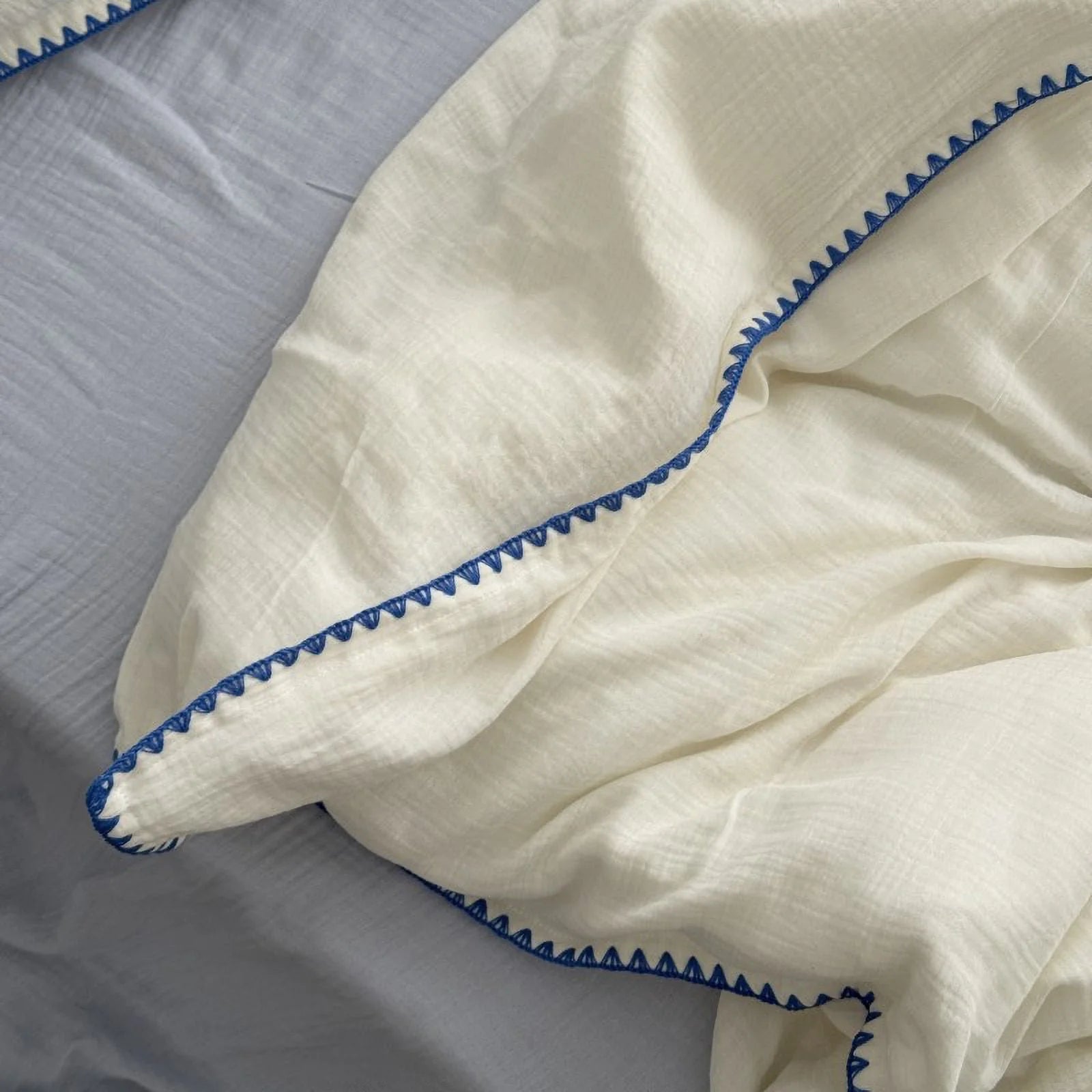 Detail shot of the cream white duvet cover with blue embroidered edge, showing the soft crinkled texture.