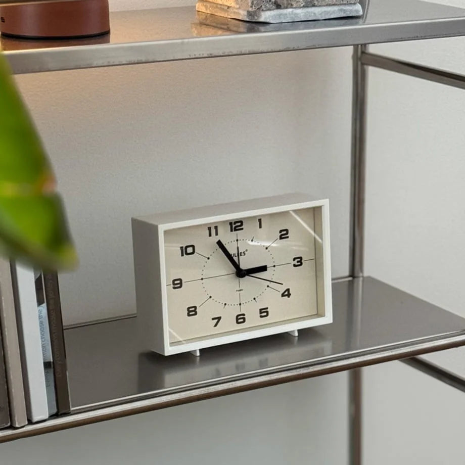 The Cream White Retro Table Clock styled on a sleek silver shelving unit.