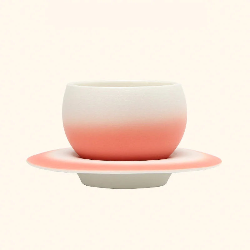 The Blush Pink Ombre Ceramic Cup displayed on its matching Saturn-ring saucer. - RoomDen