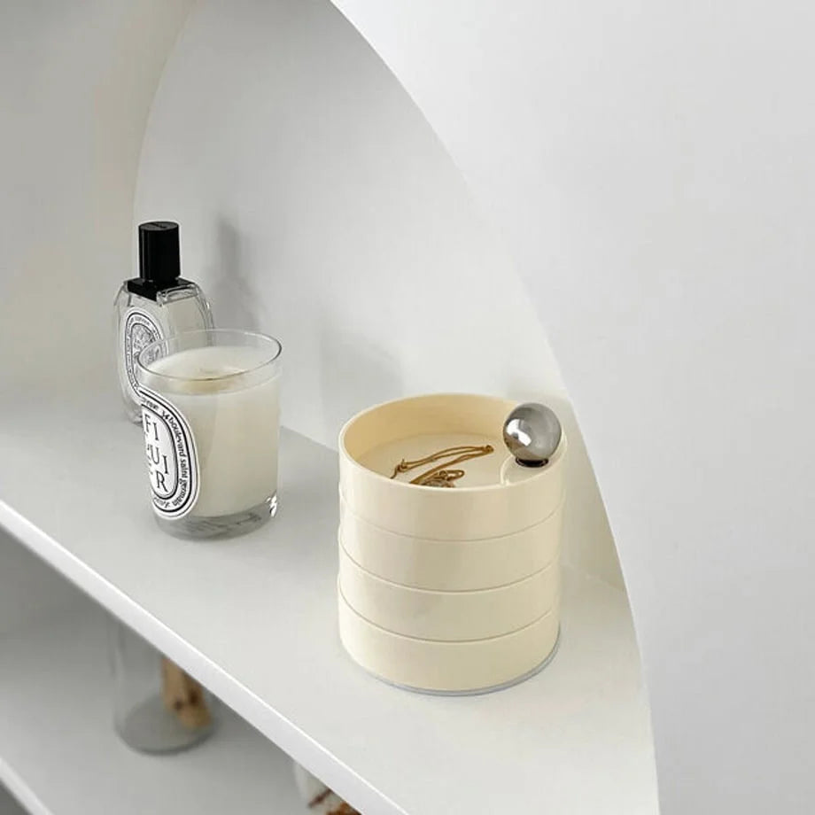 The Creamy Beige 4-tier jewelry organizer closed into a neat cylinder on a white shelf. - RoomDen