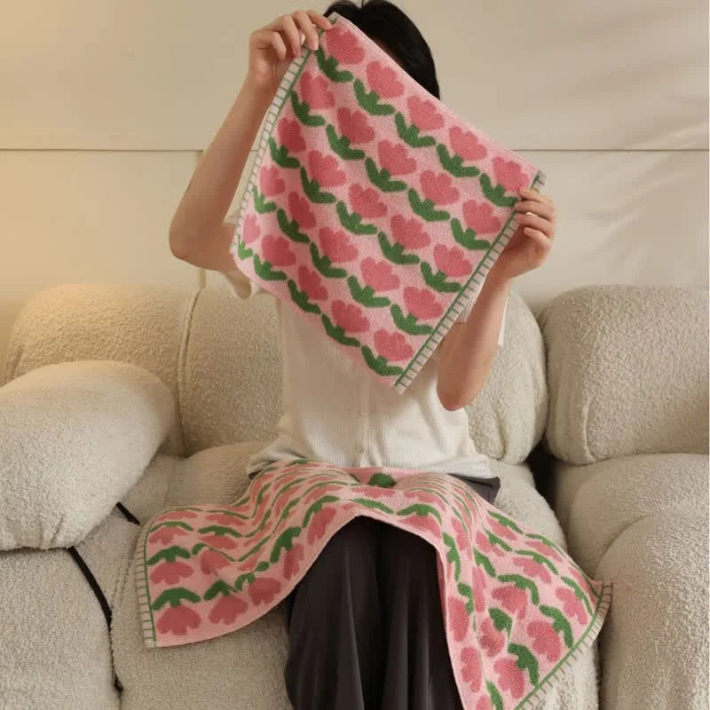 Woman holding up a pink and green floral hand towel with a matching bath towel on her lap, showcasing the set - RoomDen