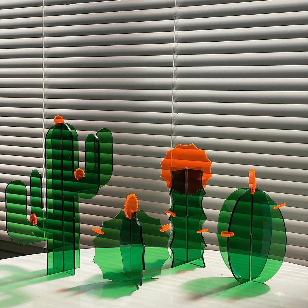 Full set of four different green acrylic cactus sculptures displayed on a white surface against window blinds - RoomDen