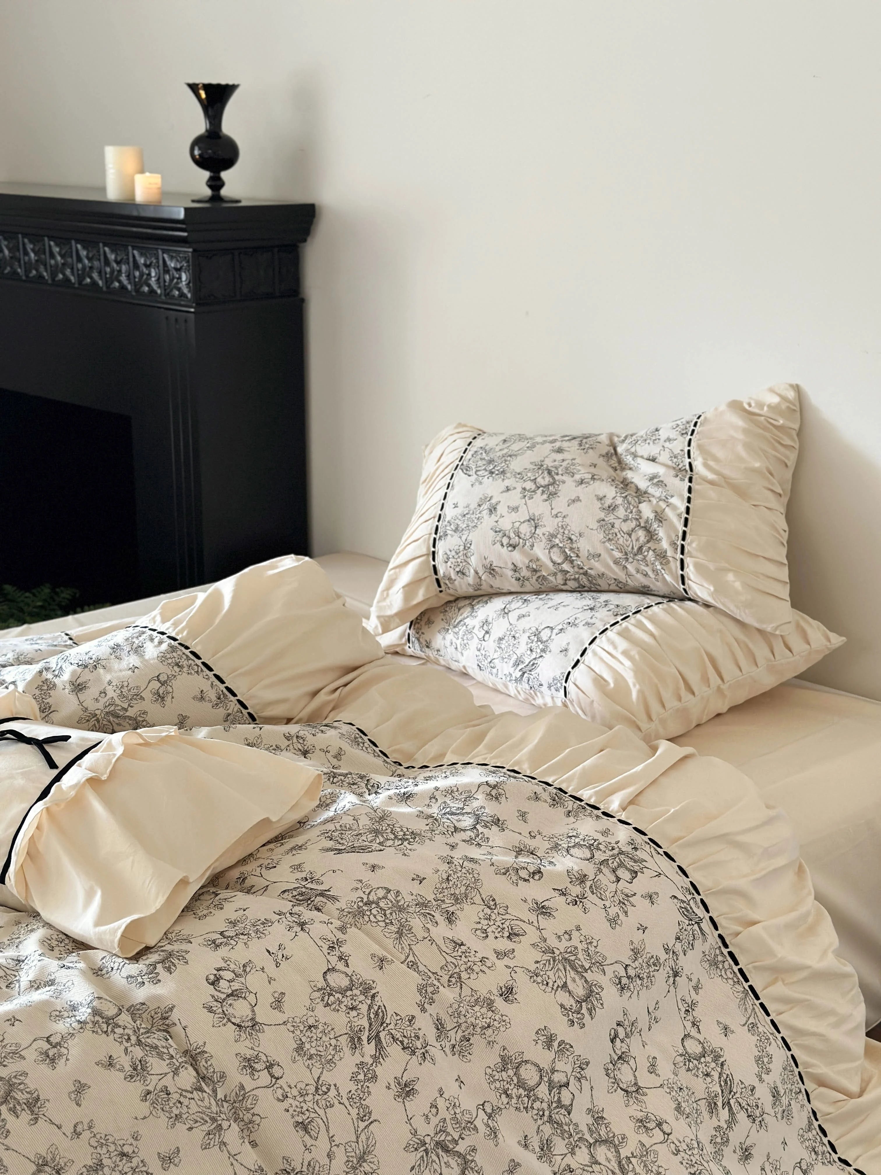 Side view of the bed with the Cream Toile set against a white wall and near a black fireplace. - RoomDen