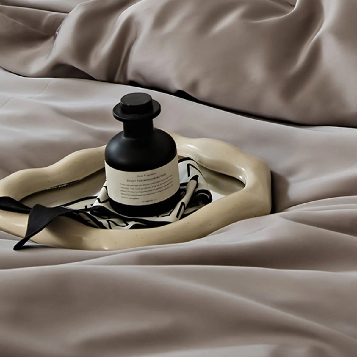 A close-up of the smooth Taupe Grey Tencel fabric with a decorative tray and perfume bottle.