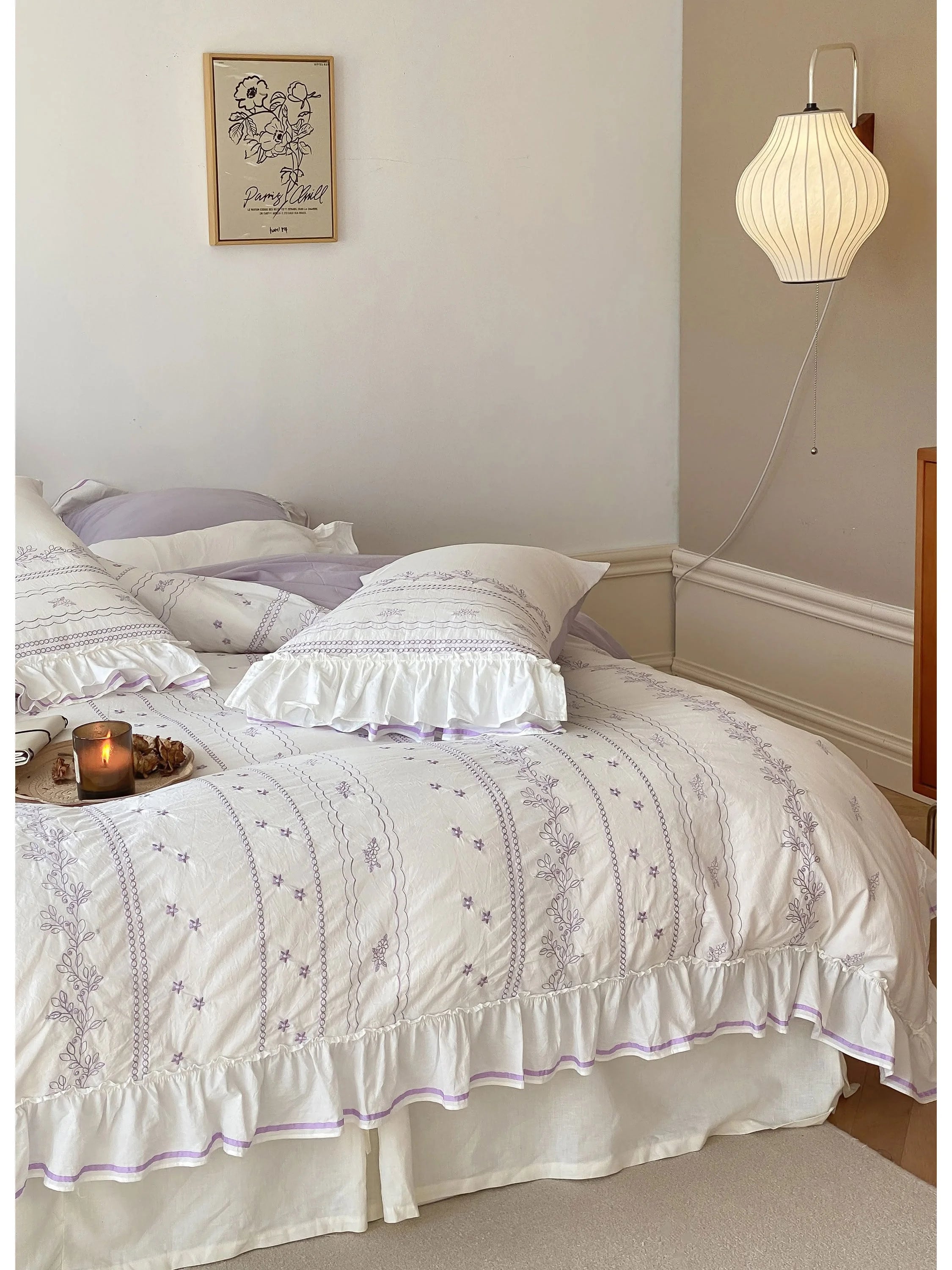 Angled shot of the Lavender embroidered bedding set, showing the ruffles and a candle on the bed.