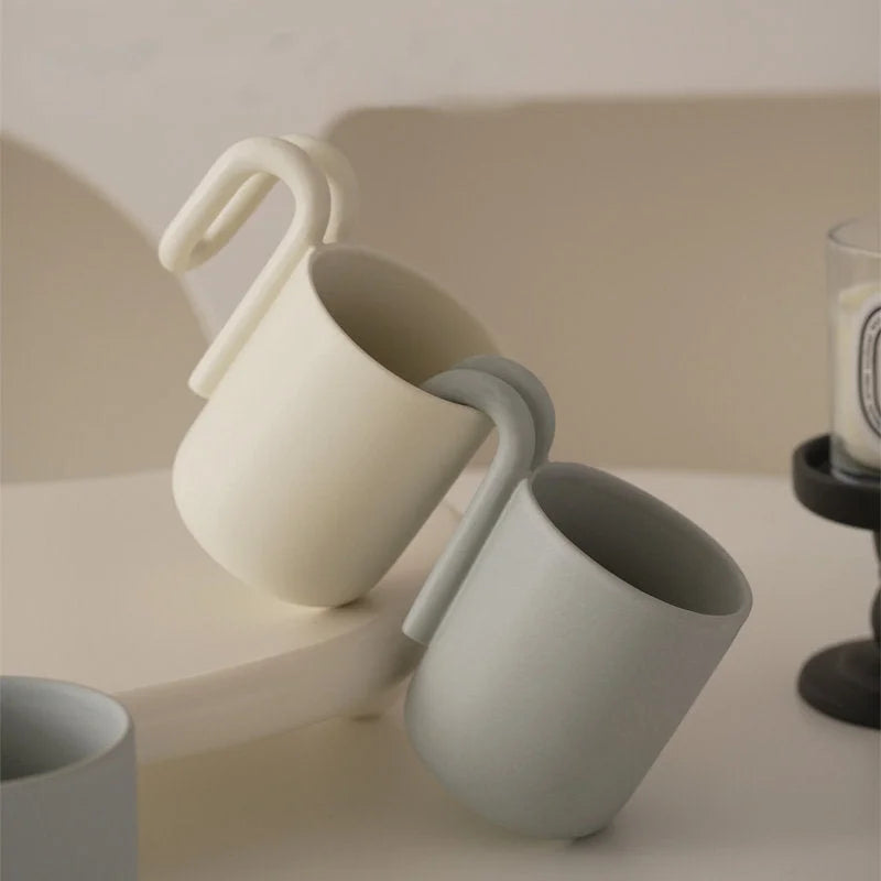 Close-up of Cream and Matte Grey sculptural handle mugs on a white surface - RoomDen