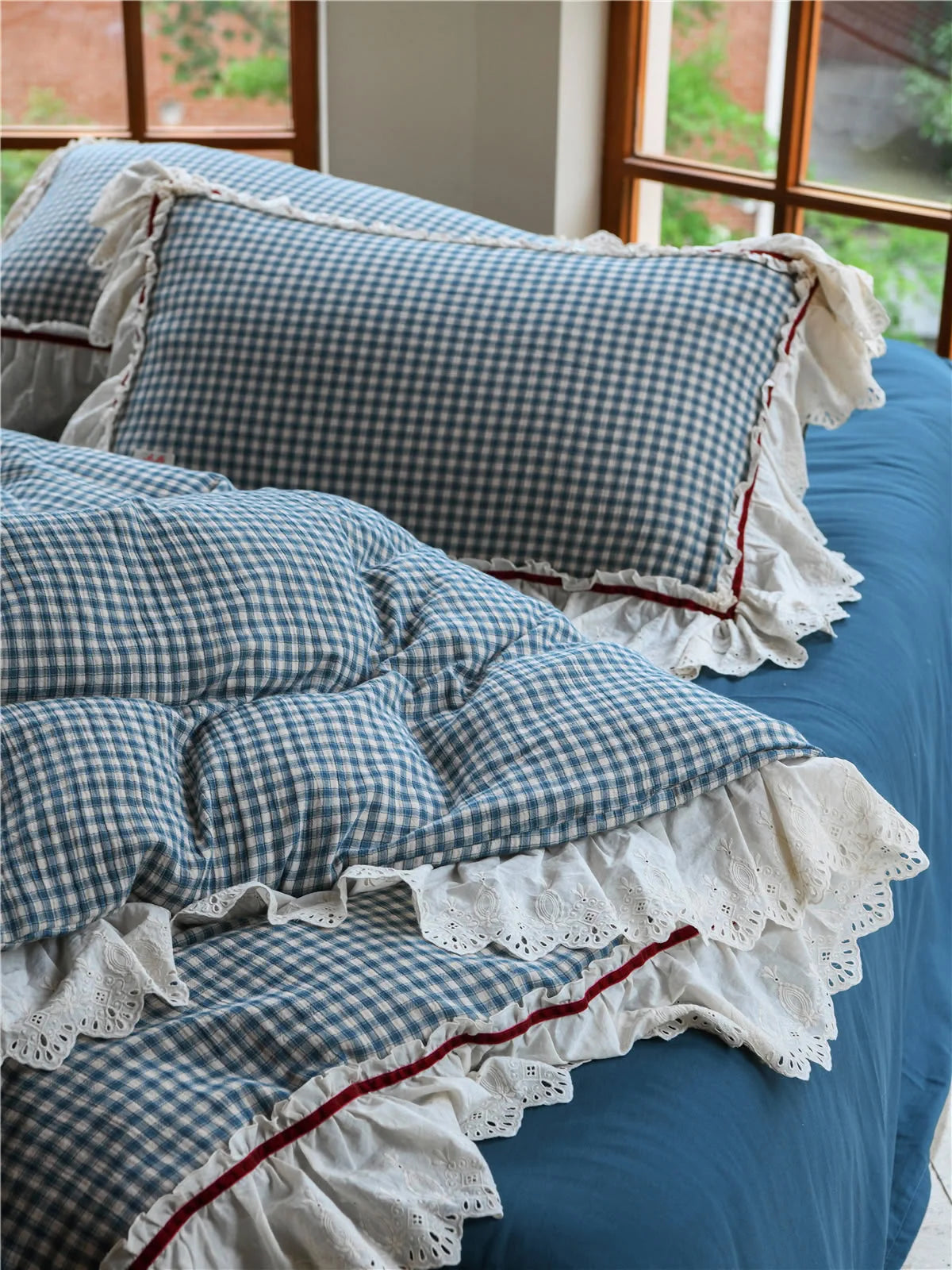 Close-up on the corner of the Blue Gingham duvet, showcasing the layered lace ruffle design against a blue sheet.