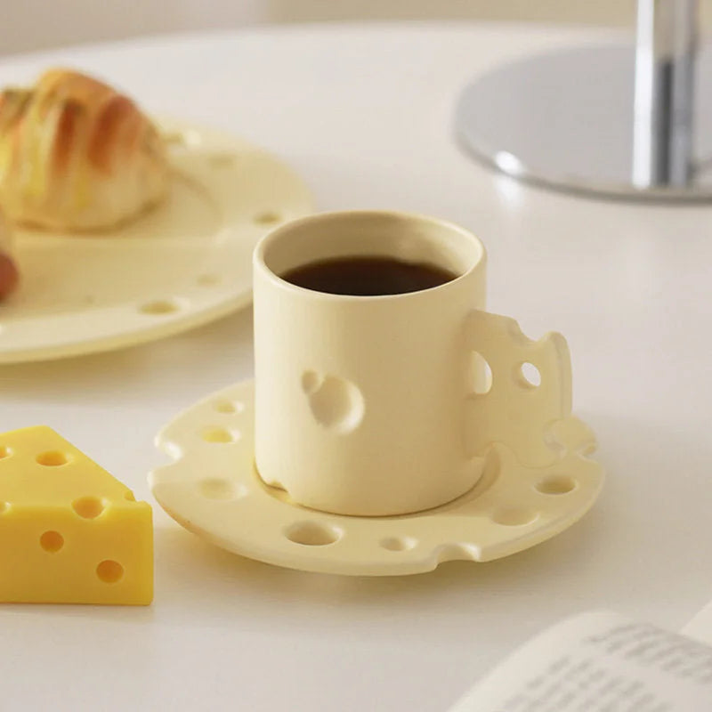 Whimsical Cheese Ceramic Mug & Saucer Set in yellow, filled with coffee on a white table. - RoomDen