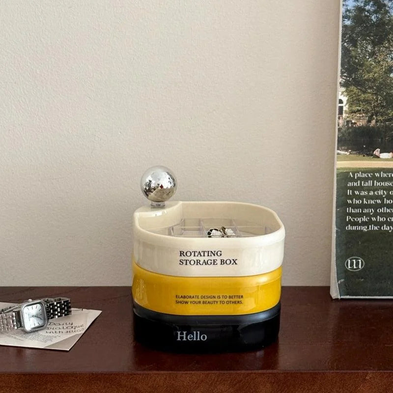 The tricolor rotating jewelry organizer sitting on a dark wood dresser next to a watch. - RoomDen