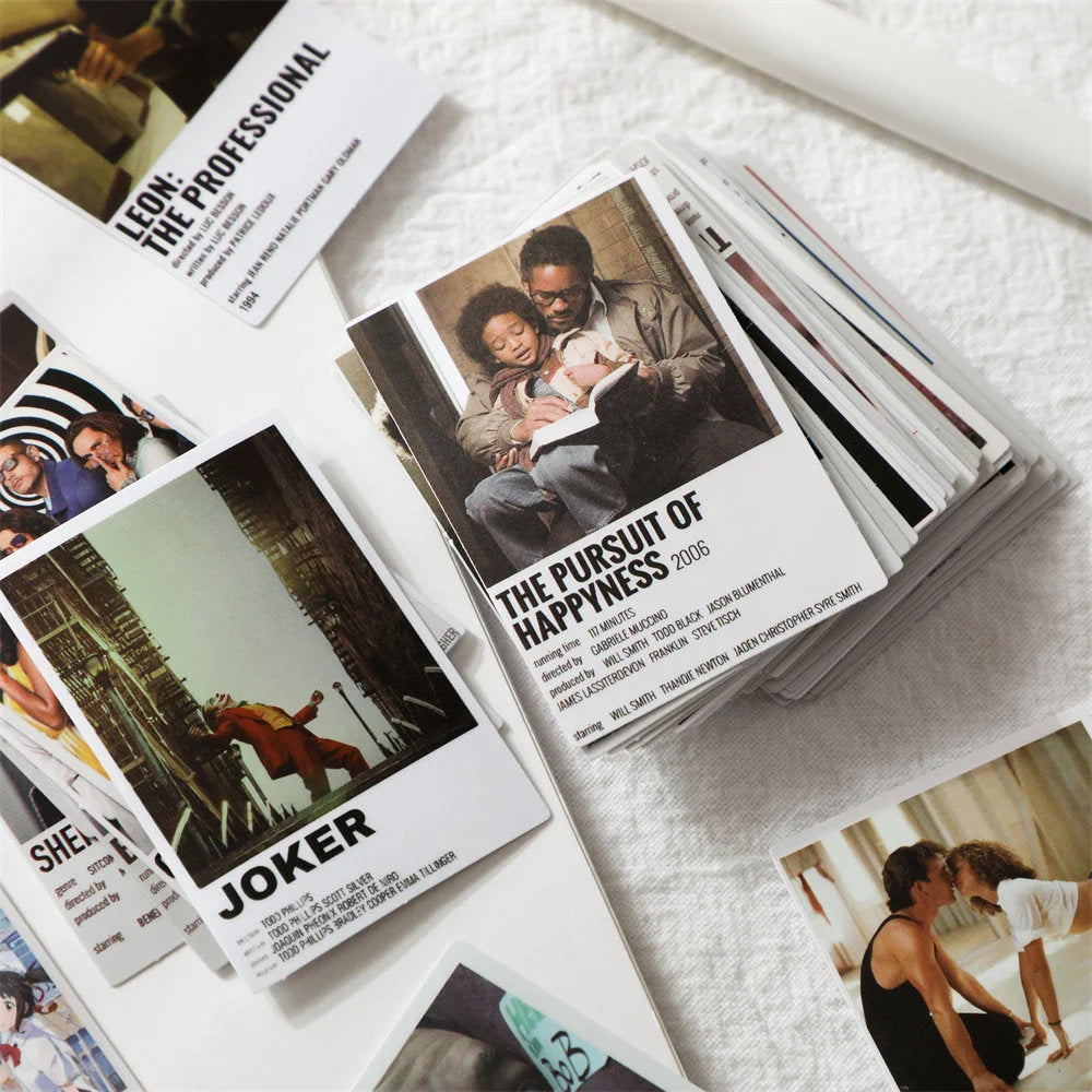 A stack of cardstock movie poster prints next to individual cards for The Pursuit of Happyness and Joker - RoomDen.