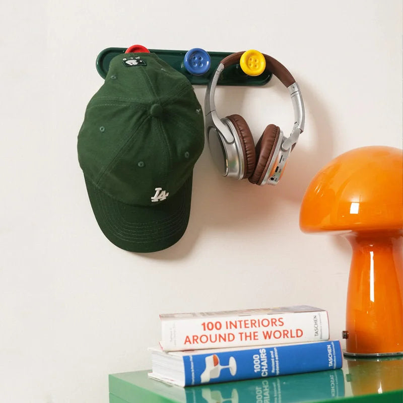 Green button wall hook rack holding a baseball cap and headphones in a stylish room. - RoomDen