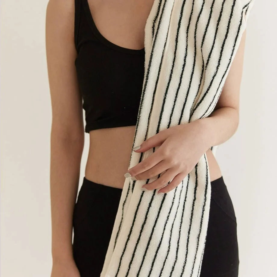 A woman in workout gear holding a folded white and black striped face towel.