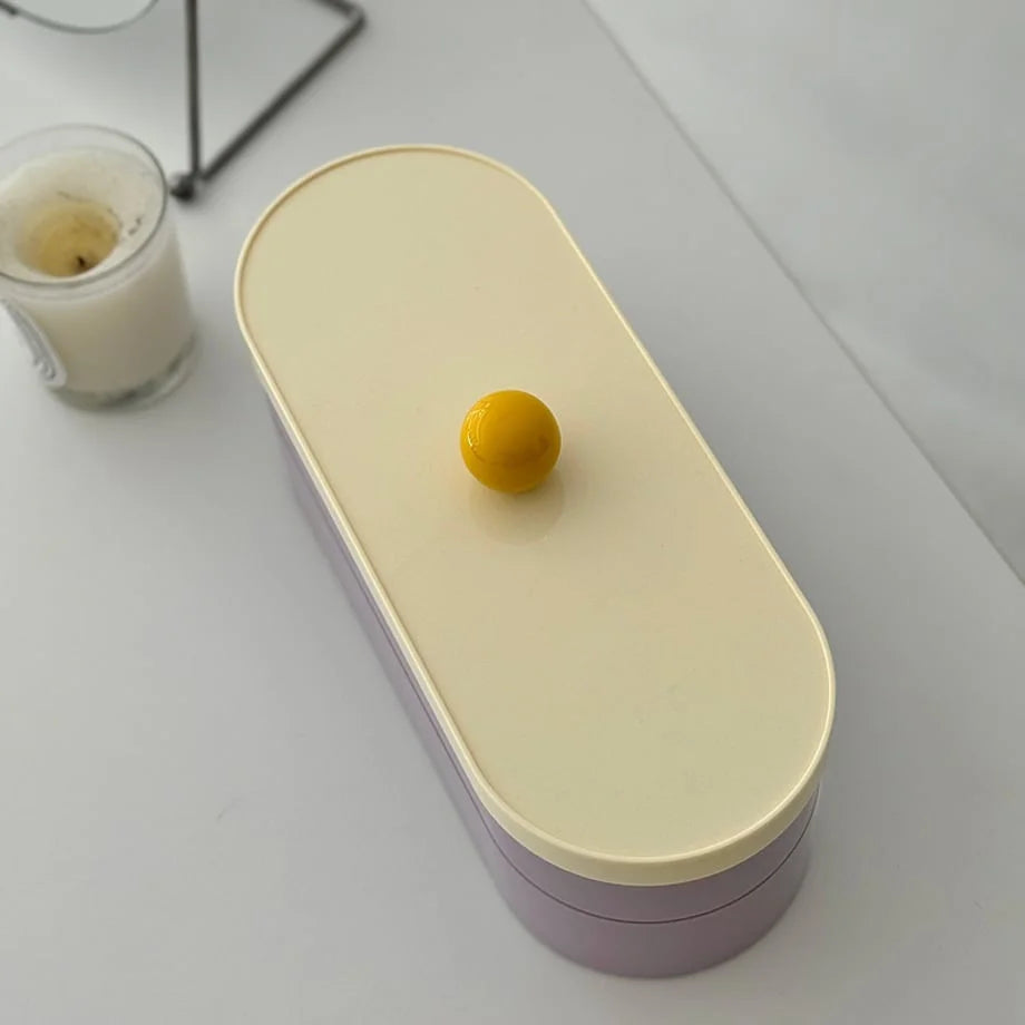 Top-down view of the oval makeup organizer, highlighting the cream lid and bright yellow knob.
