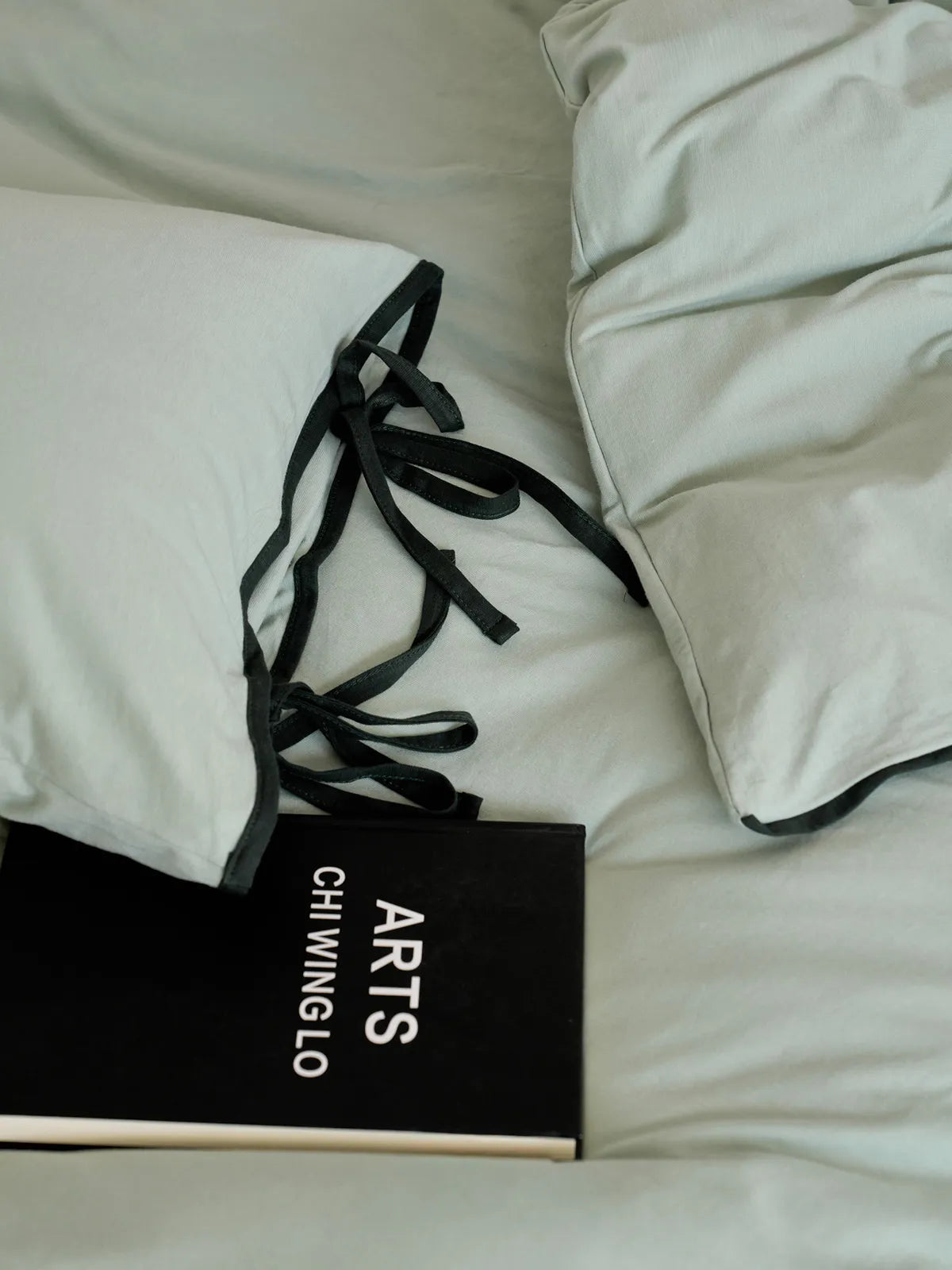 Detail shot of the black tie closure on the sage green washed cotton pillowcase. - RoomDen