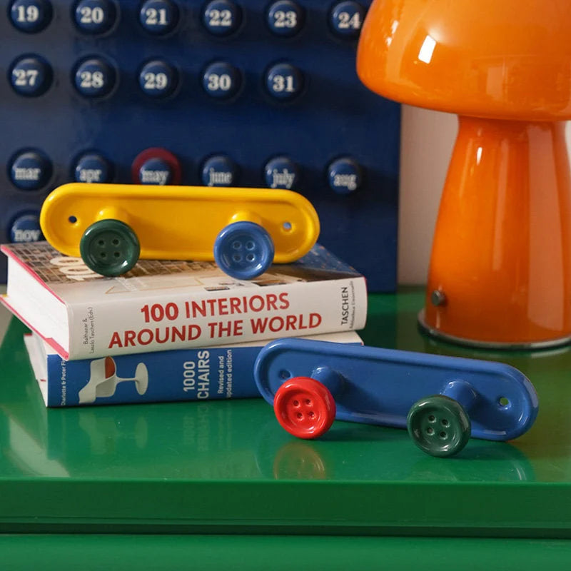 Yellow and blue button design wall hooks displayed on a stack of interior design books. - RoomDen