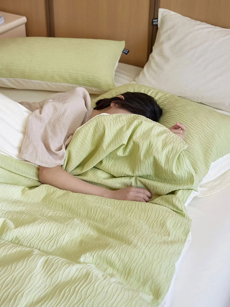 A person snuggled under the Matcha Green Wavy Textured duvet cover, showing the reverse side. - RoomDen