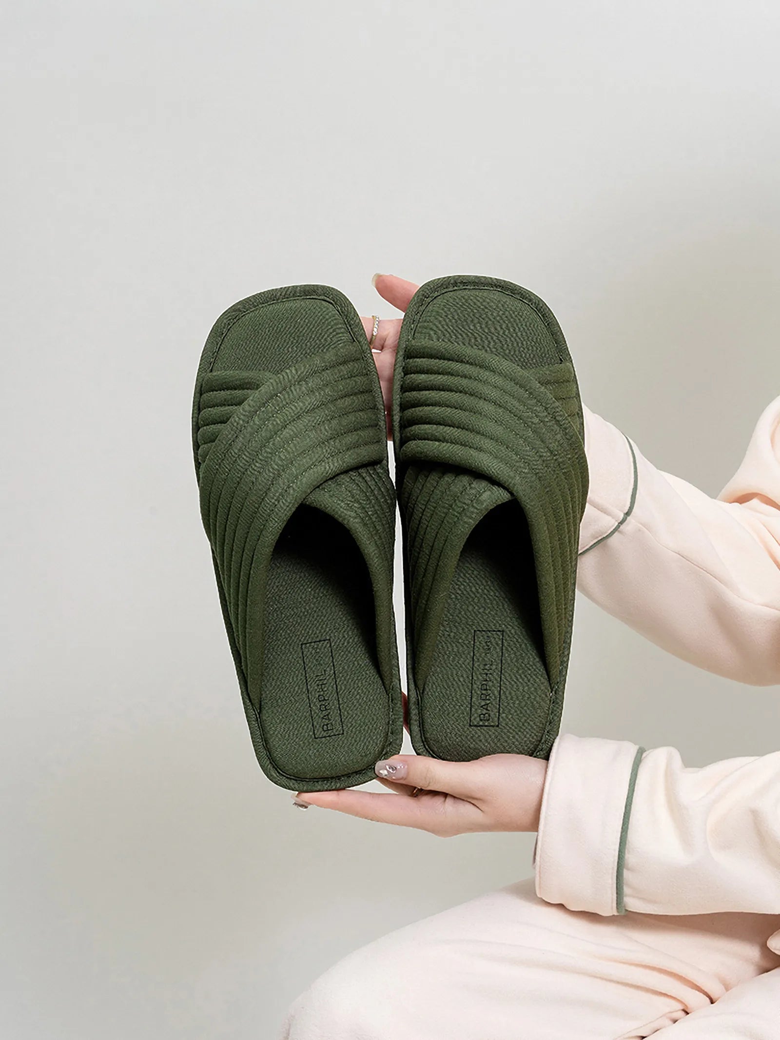 Hand holding pair of Olive Green cotton cross-strap slippers showing sole and texture