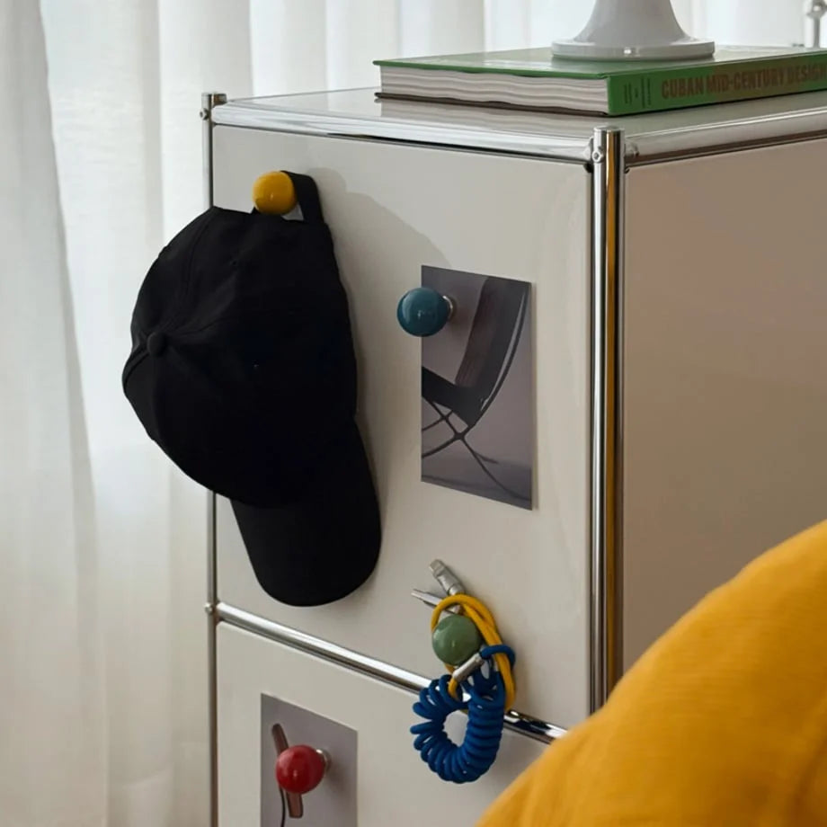 Close-up of Yellow and Blue Smooth Ball-Shaped Magnetic Hooks holding a cap and keys on a cabinet. - RoomDen