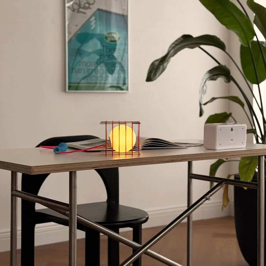 Lifestyle view of the Sunset Orange Caged Moon Lamp on a modern desk next to a plant - RoomDen
