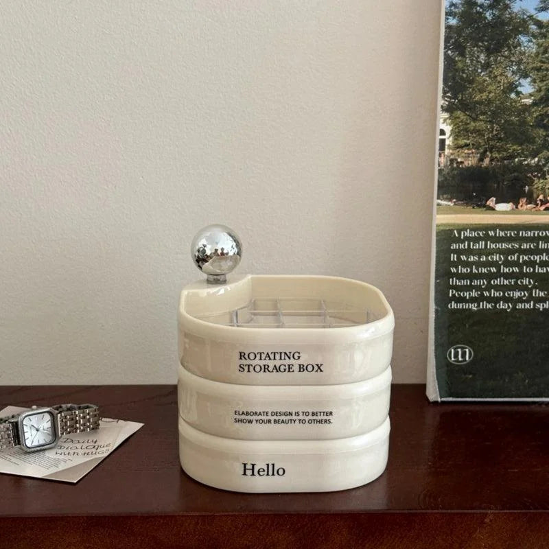The creamy white rotating jewelry organizer sitting on a dark wood dresser next to a watch. - RoomDen