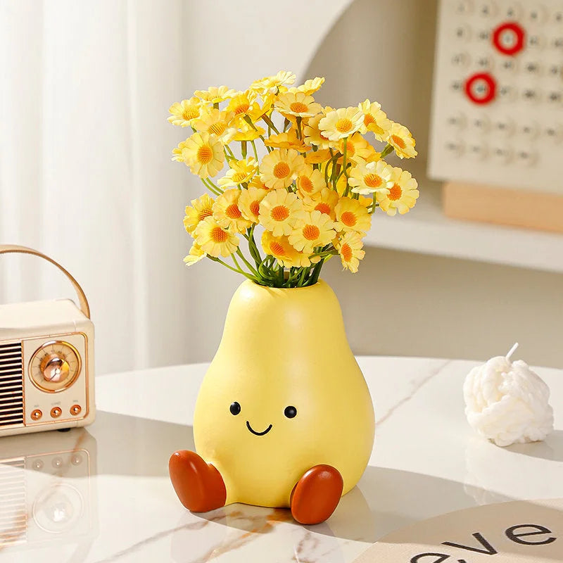 A close-up of the Cheerful Smiley Face Ceramic Pear Vase filled with yellow daisies, sitting on a white marble table - RoomDen.