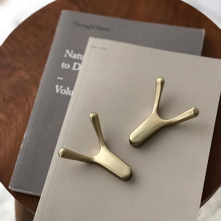 Two gold branch-shaped metal hooks displayed on top of minimalist grey books on a wooden table - RoomDen