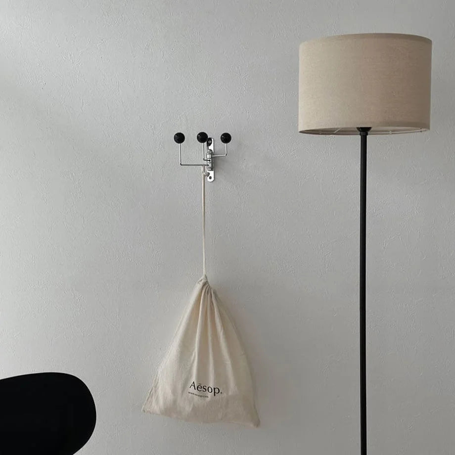 Lifestyle view of the black swivel wall hook holding an Aesop tote bag next to a floor lamp - RoomDen.