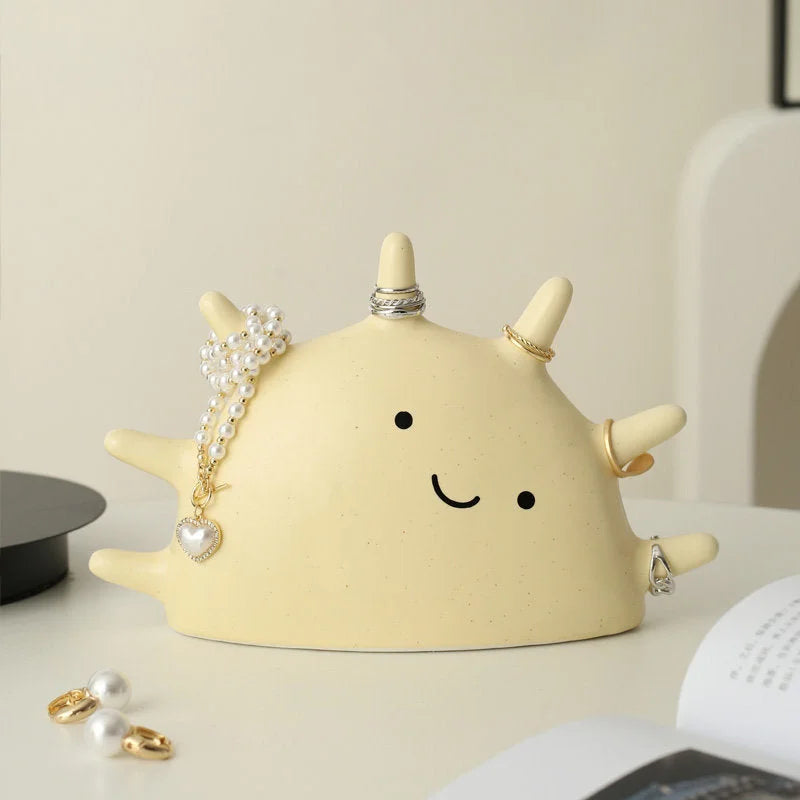 Front view of the Creamy Beige Smiling Sun Jewelry Organizer holding various rings and a pearl necklace on a desk - RoomDen