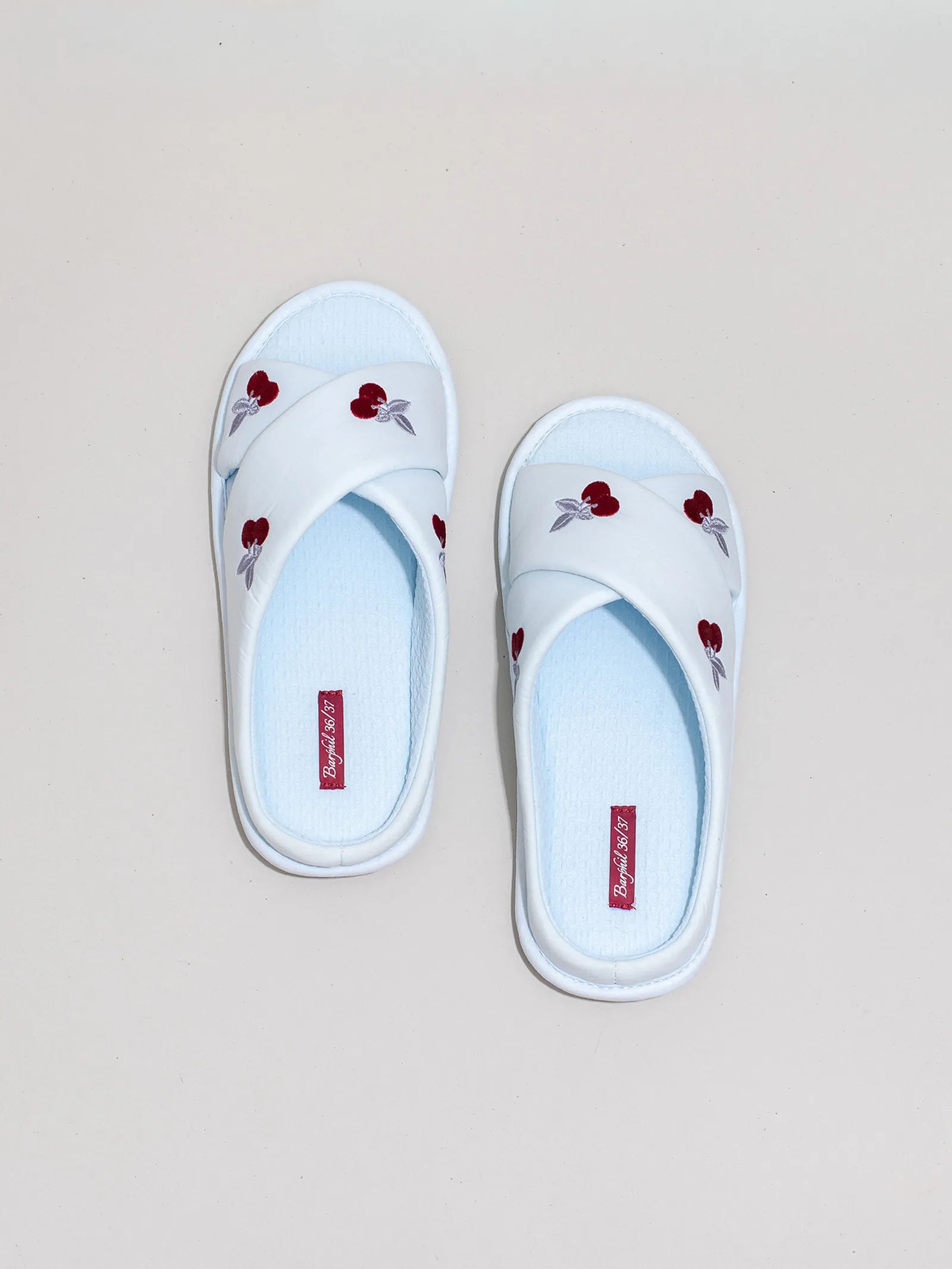 White embroidered cherry slippers angled on white block - RoomDen