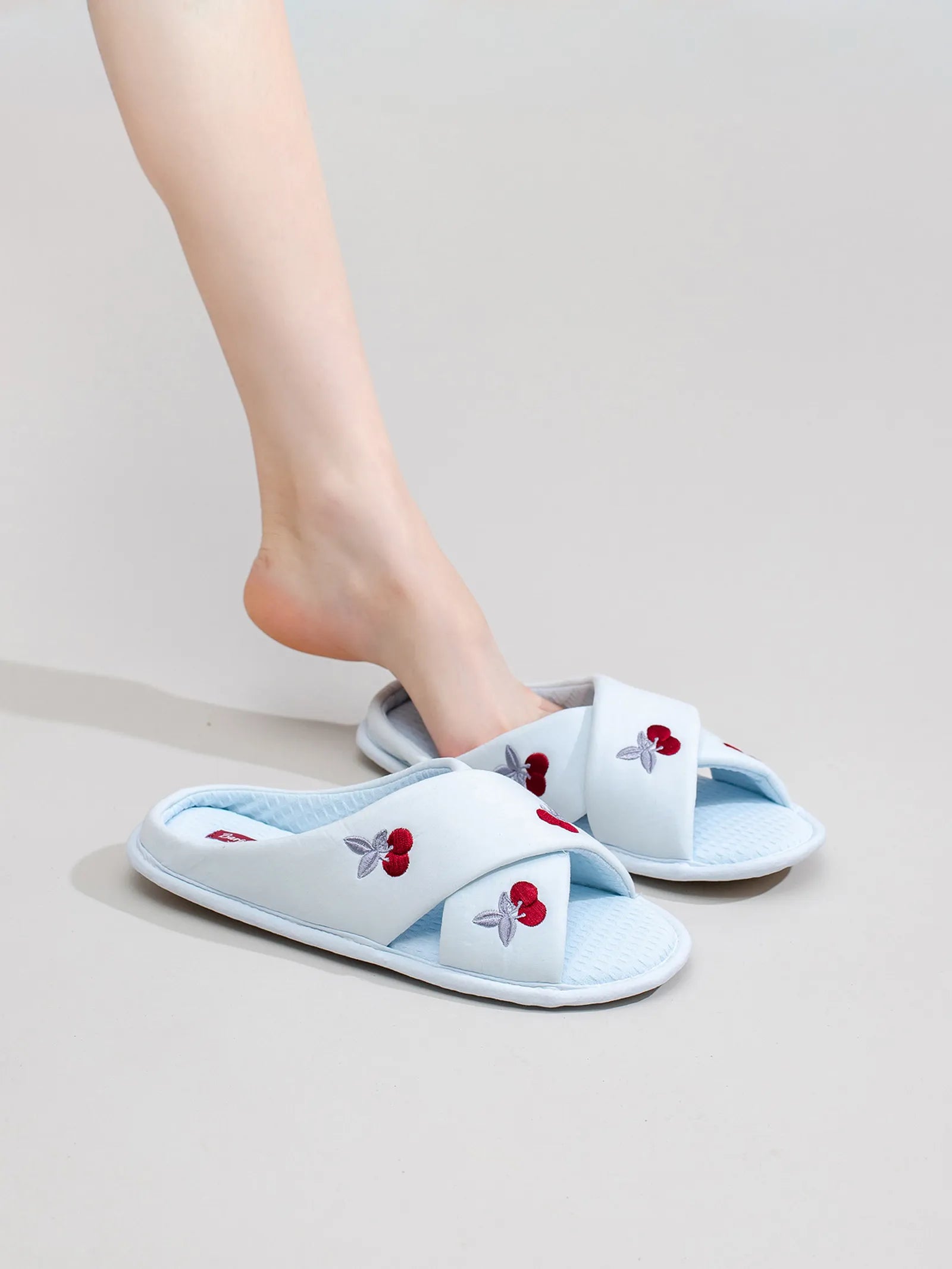 Model wearing light blue cross-band slippers with cherry embroidery on leg - RoomDen