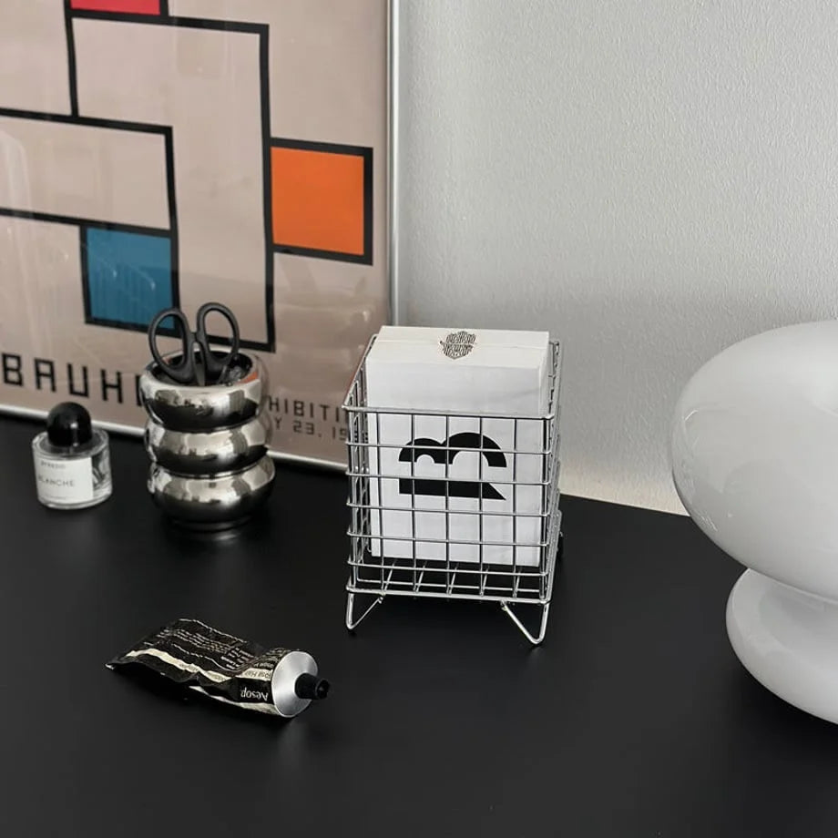 Close-up of the metal wireframe organizer holding white boxes, placed on a dark desk with other accessories - RoomDen.