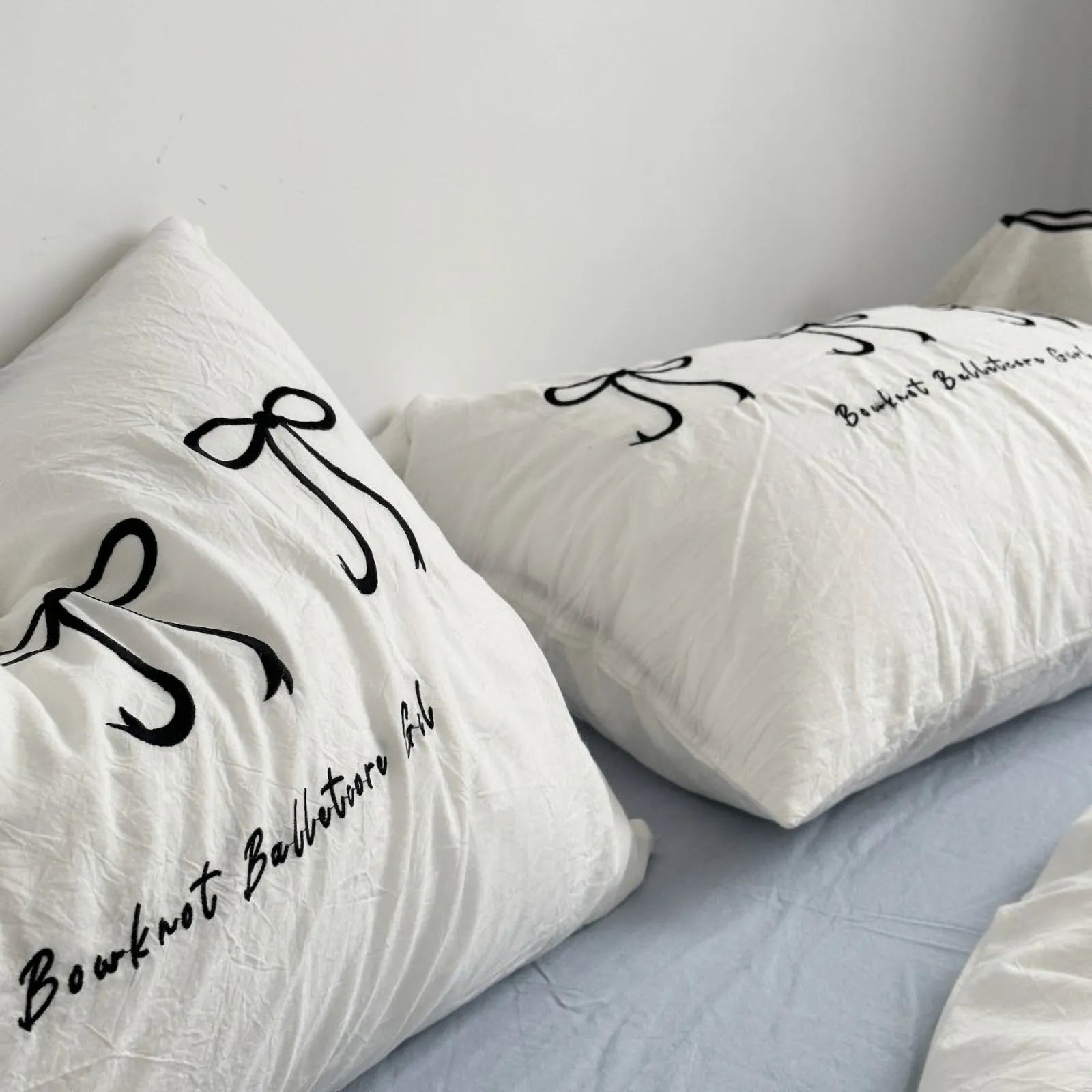 Close-up of pillows on a white bedding set, showing the detail of the black embroidered "Bowknot Balletcore Girl" text and bow design.