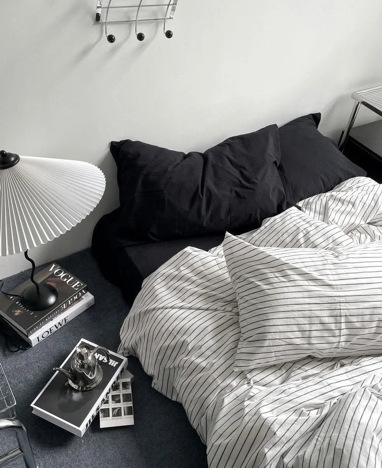 Angled view of the pinstripe washed cotton bedding, highlighting the contrast with solid black pillows in a minimalist bedroom. - RoomDen