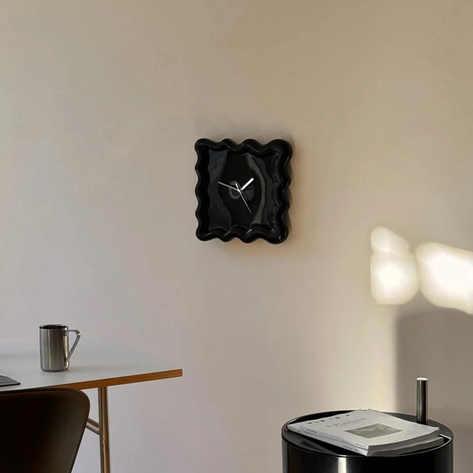 Lifestyle view of the black Wavy Squiggle Clock on a wall, with a desk and metal mug in the foreground. - RoomDen
